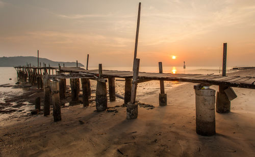 Wooden posts on beach against sky during sunset