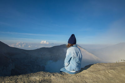 Rear view of woman sitting on mountain against sky