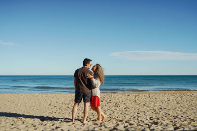 Rear view of woman with man standing at beach against clear sky