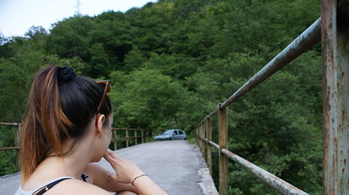 Side view of young woman sitting on bridge leading towards forest