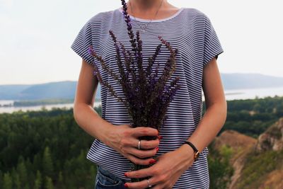 Midsection of woman holding plants while standing against sky