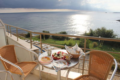 Chairs and table by sea against sky seen from balcony