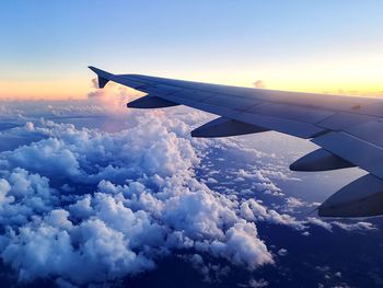 Airplane flying over cloudscape against sky during sunset