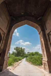 Road amidst trees against sky seen through archway