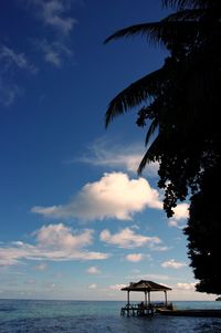 Thatched hut over water against cloudy sky