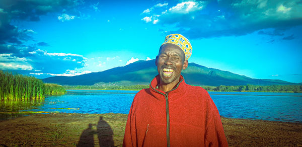 Portrait of smiling man standing by lake against sky