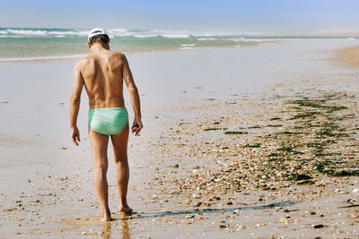Full length rear view of shirtless man walking at beach