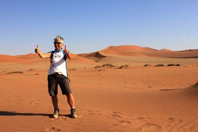 Full length of smiling woman gesturing while standing on sand dune