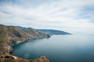 Scenic view of mountains by sea against cloudy sky