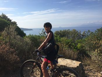 Portrait of mature woman riding bicycle by plants on field against sky