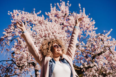 Portrait of happy hispanic woman with afro hair in spring among pink blossom flowers. sunny nature