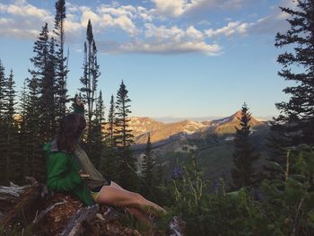 Side view of female hiker sitting at mountain peak against sky