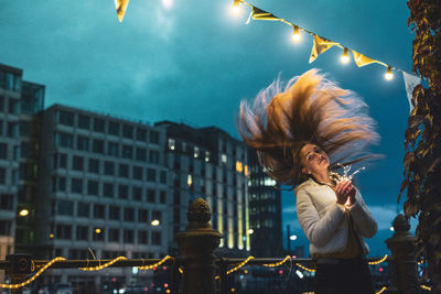 Young woman with tousled hair holding illuminated string light at night