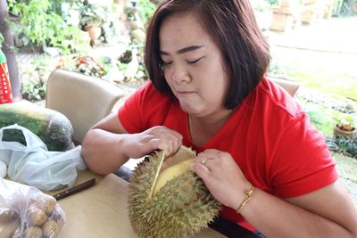 Woman opening durian on table sitting in yard