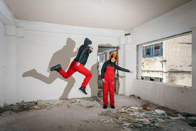 Woman gesturing while man jumping in abandoned building