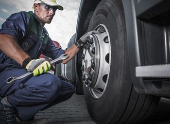 Full length of worker examining truck tire