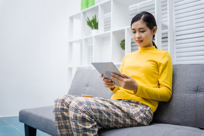 Young woman using mobile phone while sitting on sofa at home