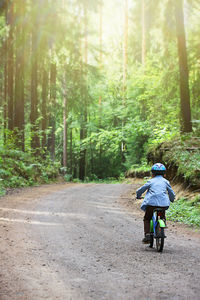 Rear view of person riding bicycle on dirt road