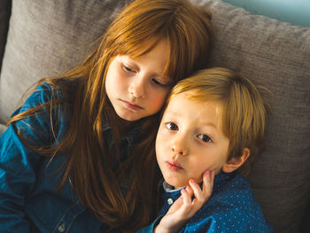 High angle view of siblings sitting on sofa at home