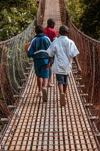 Rear view of three boys crossing a bridge carrying a football 
