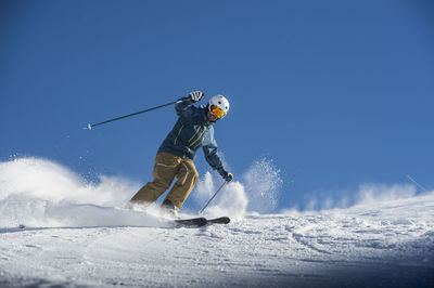 Young man skiing on snow against blue clear sky