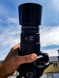 Close-up of hand holding camera against sky