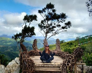 Portrait of man sitting on tree against sky