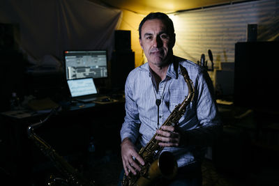 Smiling musician with saxophone sitting in recording studio