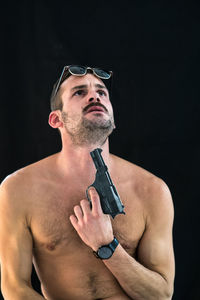 Shirtless man attempting suicide with gun against black background