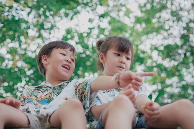 Low angle view of cute siblings sitting against trees