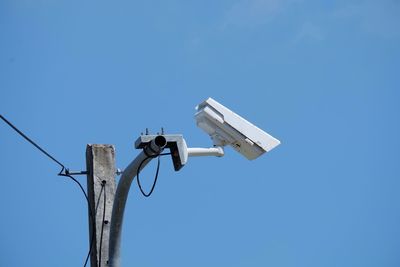 Low angle view of security camera against clear blue sky