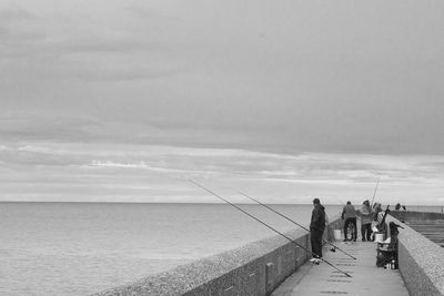 People fishing in sea against sky