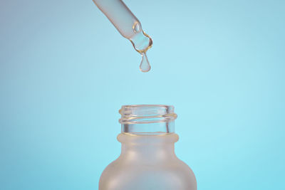 Face serum oil drop with dropper glass bottle pipette on blue background close up