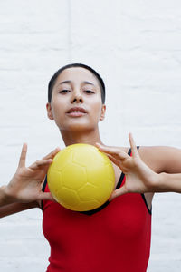 Portrait of smiling young woman holding soccer ball at home