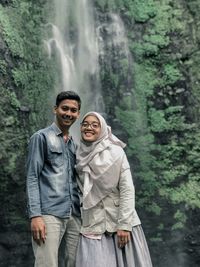 Portrait of couple smiling while standing against waterfall