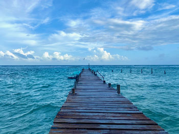 Wooden jetty leading to pier over sea against sky