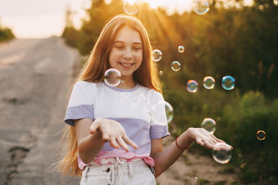 Portrait of smiling girl playing with bubbles in park during sunset