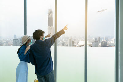 Rear view of man and woman standing by glass window