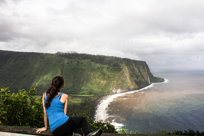 Woman standing on cliff by sea against sky