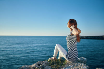 Young woman looking at sea against clear blue sky