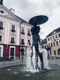 Full length of woman splashing water in city against sky