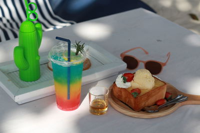 High angle view of colorful juice and honey toast and sunglass on table beach day concept