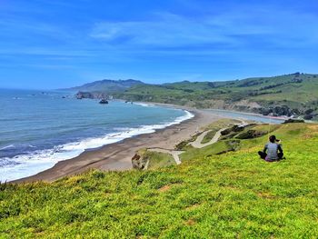 Rear view of young woman on cliff above beach and ocean against sky