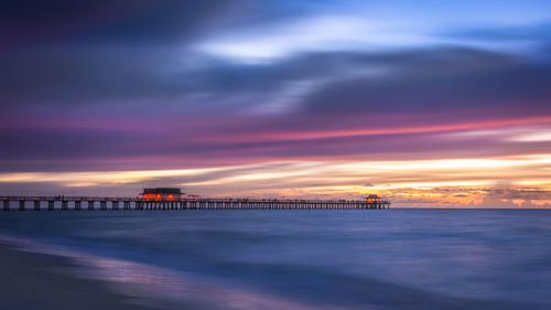 Pier over sea against dramatic sky during sunset