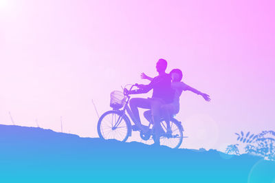 Silhouette people riding bicycle against sky