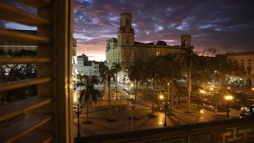 Illuminated street amidst buildings against sky at dusk