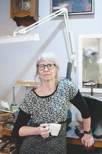 Portrait of confident senior woman holding coffee cup in jewelry shop