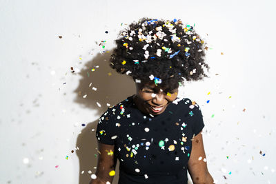 Smiling woman with confetti falling on head standing against white background