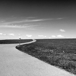 Scenic view of road by field against sky