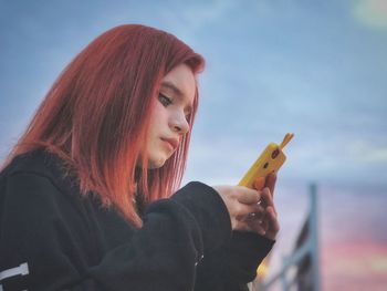 Close-up of young woman using smart phone against sky